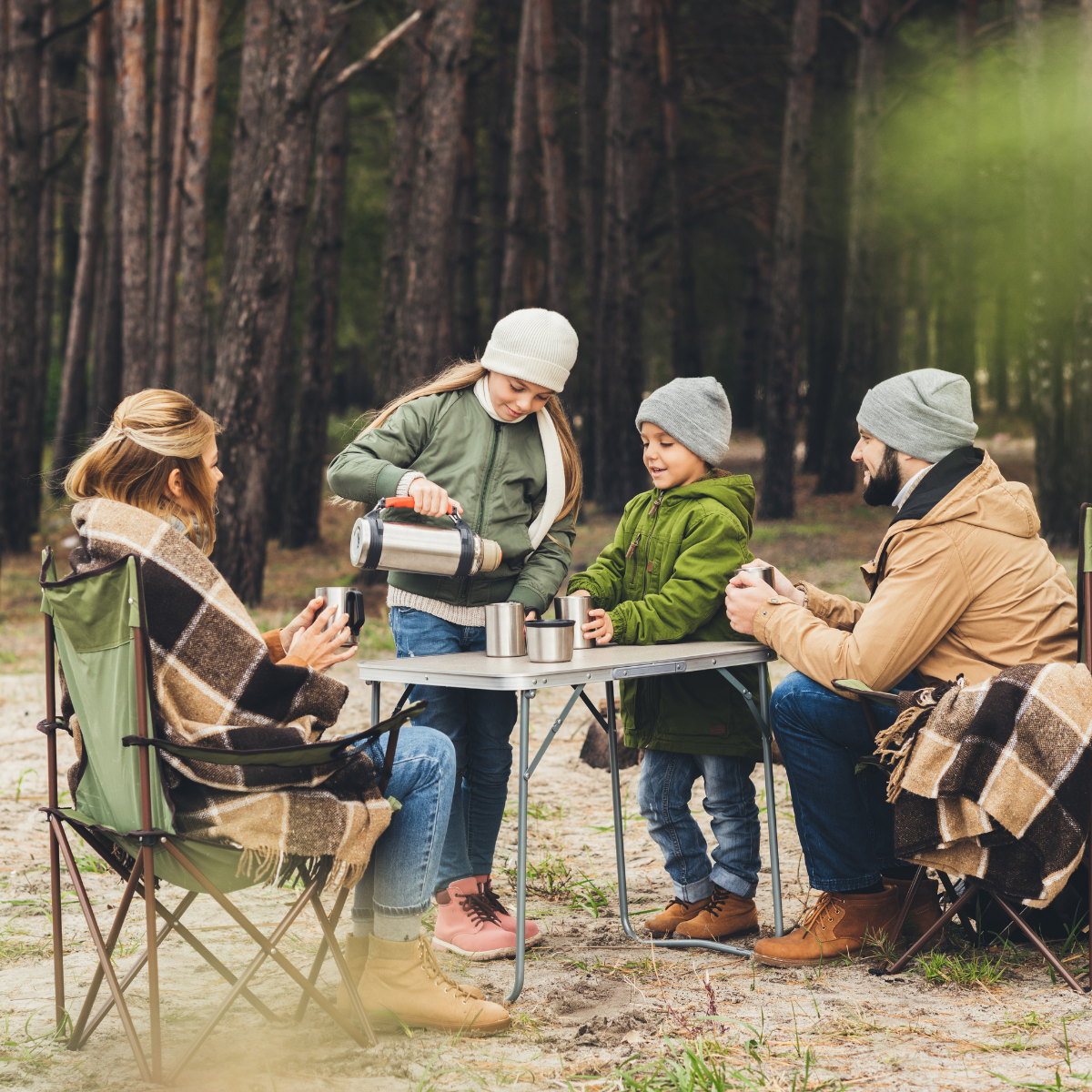 Familj sitter vid campingbordet i skogen och fikar tillsammans, enkel camping med barn